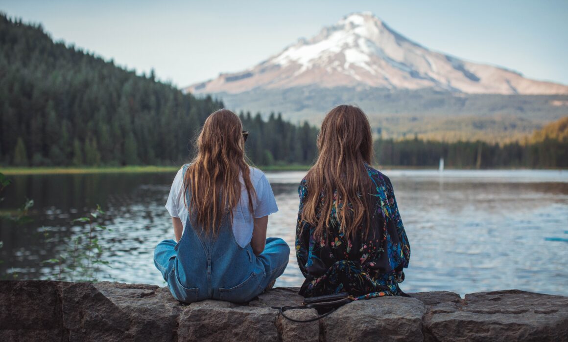 Two women sitting in front of a lake, possibly discussing an apology.